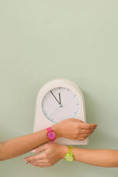 Female hands with watches and clock on color background