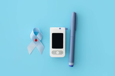 Renk arkaplanında glukometre ve şırıngayla farkındalık kurdelesi. Diyabet kavramı