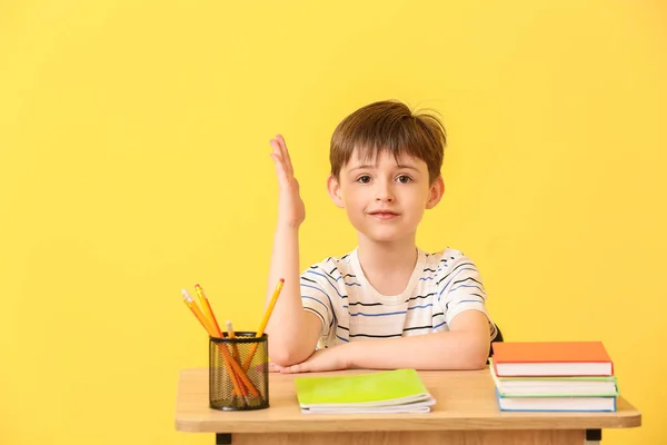 Cute Ucznia Podniesioną Ręką Siedzi Przy Biurku Tle Koloru — Zdjęcie stockowe
