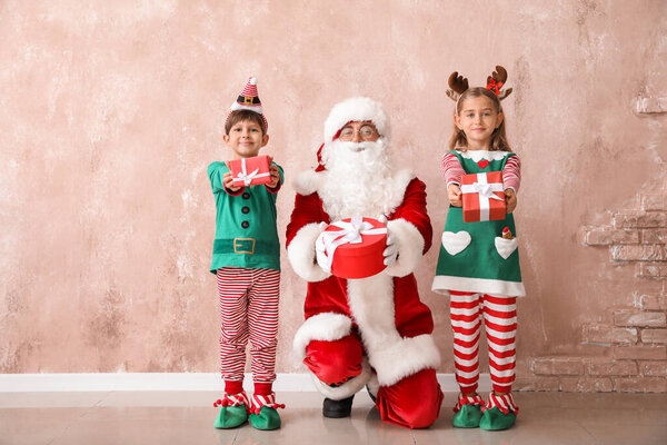 Cute little elves with Santa Claus and Christmas gifts near color wall