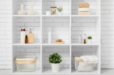 Banyo aksesuarları ve beyaz tuğla duvarın yanında bitkileri olan raf ünitesi.