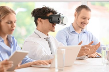 Genç işadamı ofisinde iş arkadaşlarıyla VR gözlükleri kullanıyor.
