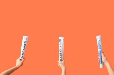 Turuncu arka planda sarılmış gazeteleri olan kadınlar