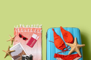 Bavul, mayo, dergi ve plaj aksesuarları yeşil arka planda, yakın plan