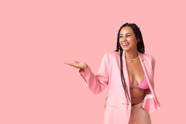 Sexy young African-American woman with braids showing something on pink background