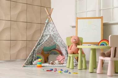 Çocuk odasının içinde masa, çadır ve oyuncaklar var.