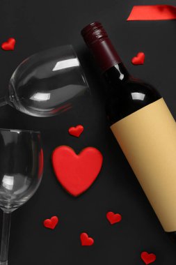 Bir şişe şarap, siyah arka planda bardaklar ve kalpler. Sevgililer Günü kutlaması