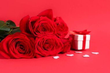 Roses with gift box and hearts on red background