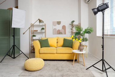 Photo shoot of living room with yellow sofa, shelf units and lighting equipment in studio