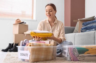Genç bir kadın evde bağışlanmak üzere giysilerini konteynıra koyuyor.