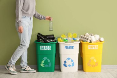 Yeşil duvarın yanındaki çöp kutularına farklı atık tipleri koyan bir kadın. Geri dönüşüm kavramı
