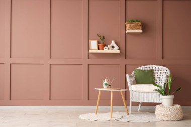 Masa, puf ve hasır koltuk, odanın içindeki kahverengi duvarın yanında.