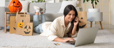 Cep telefonu ve dizüstü bilgisayarı olan genç bir kadın Cadılar Bayramı için internetten alışveriş yapıyor.