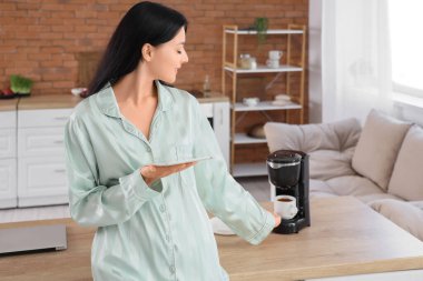 Tablet bilgisayarlı genç bir kadın mutfakta kahve içiyor.