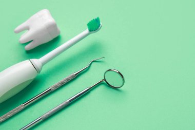 Elektrikli diş fırçası, diş aletleri ve yeşil arka planda diş modeli. Dünya Diş Hekimi Günü