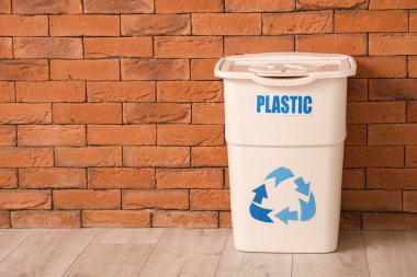 Tuğla duvarın yanında PLASTIC işareti olan boş çöp kutusu. Geri dönüşüm kavramı