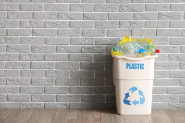 Gri tuğla duvarın yanında PLASTIC işareti olan tam çöp kutusu. Geri dönüşüm kavramı