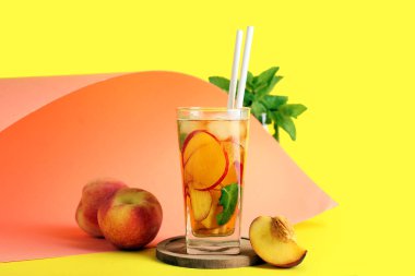 Sarı arka planda nane ve şeftalili bir bardak lezzetli buzlu çay.