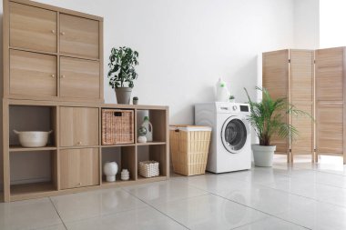 Çamaşır makinesi, sepeti ve raf ünitesi olan hafif çamaşır odasının içi.