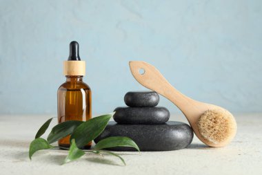 Spa taşlı kompozisyon, yeşil dal ve mavi duvarın yanındaki beyaz masada bir şişe kozmetik ürünü.