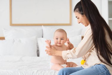 Anne küçük bebeğine yatak odasında masaj yapıyor.