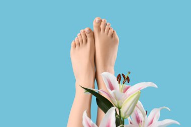 Taze pedikür ve mavi arka planda zambak çiçekleri olan genç bir kadının ayakları, yakın plan.