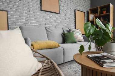 Modern oturma odasının içinde rahat gri bir kanepe ve tuğla duvarın yanında bir sehpa.