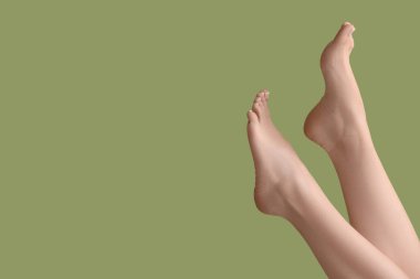 Feet of young woman with fresh pedicure on green background, closeup