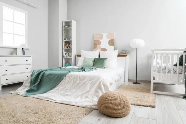 Interior of light room with baby crib, bed and shelf unit