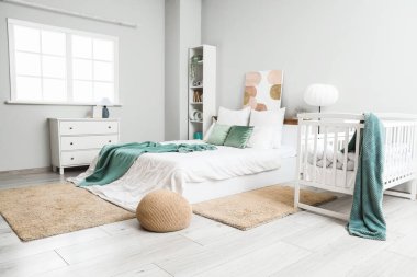 Interior of light room with baby crib, bed and shelf unit