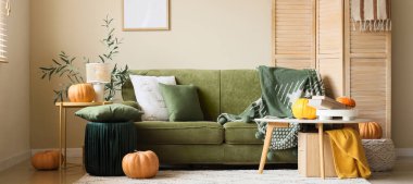 Yeşil kanepeli, masalı ve balkabaklı aydınlık oturma odasının içi.