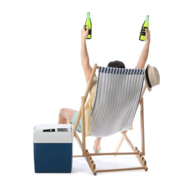 Young man with portable fridge and bottles of cold beer sitting on deckchair isolated on white background, back view