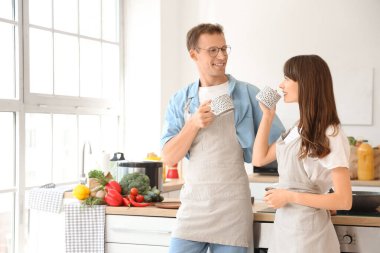 Young couple with aprons and cups of tea in kitchen