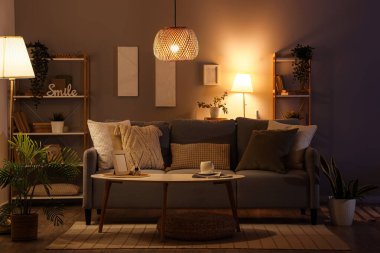 Interior of dark living room with glowing lamps, sofa and shelf units in evening