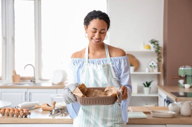 Young African-American woman holding baking dish with tasty cookies in kitchen