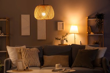 Interior of dark living room with glowing lamps, sofa and plants in evening