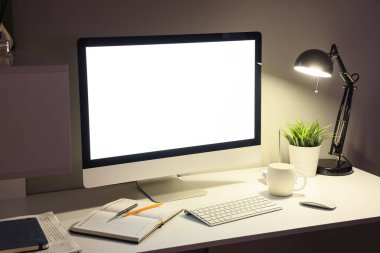 Boş bilgisayar monitörü ve karanlık ofiste parlayan lambası olan işyeri