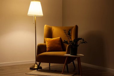 Interior of dark living room with glowing lamp, armchair and table in evening
