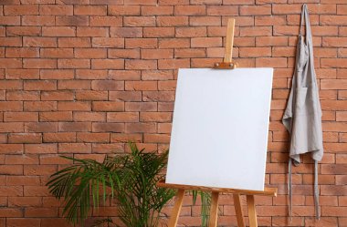 Kahverengi tuğla duvarın yanında boş tuval olan ahşap sehpa