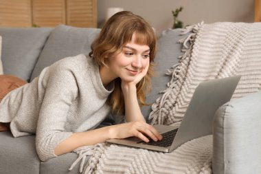 Dizüstü bilgisayarı olan genç bir kadın evdeki kanepede dinleniyor.