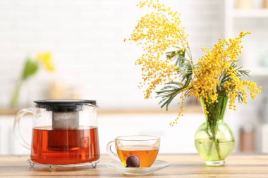 Çaydanlık ve bir fincan siyah çay. Mutfaktaki masada mimoza var.