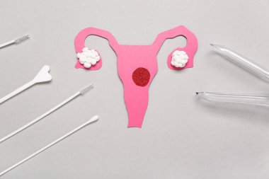 Pap smear test araçları ve gri arka planda jinekolojik spekulum içeren kağıt rahim.