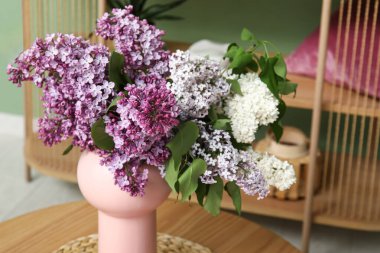 Süslü oturma odasındaki sehpanın üzerinde leylak dalları olan vazo, yakın plan.