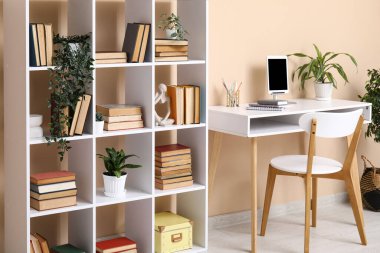 Çalışma odası ve bej duvarın yanında kitaplığı olan modern oturma odasının içinde.