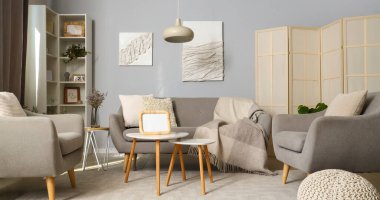 Modern oturma odasının içinde gri kanepe, koltuklar ve sehpanın üzerinde boş fotoğraf çerçevesi.