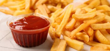 Tasty french fries and plastic bowl of ketchup on table, closeup