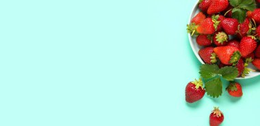 Plate of fresh ripe strawberries on turquoise background with space for text, top view
