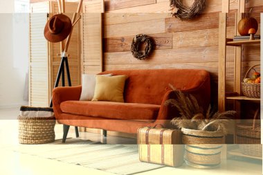 Oturma odasının içinde kahverengi kanepe, raf, çelenk ve balkabakları raflarda.