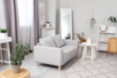 Açık renkli oturma odası, gri kanepe, sehpa ve halı, bulanık manzara.