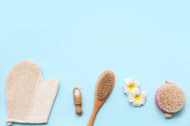Exfoliating glove, plumeria flowers, massage body brushes and scoop with sea salt on blue background
